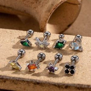 Set of 8 stainless steel cartilage studs with colorful zircons on a rustic stone background