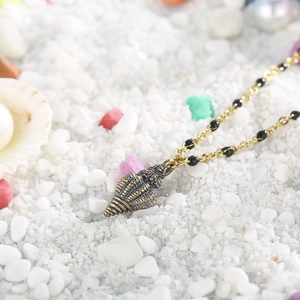 Macro detail of bronze conch shell pendant and black beads on a beach background