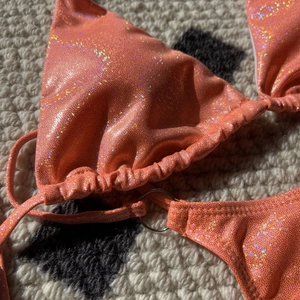 Macro view of bright orange glitter bikini fabric with silver ring and lace-up details