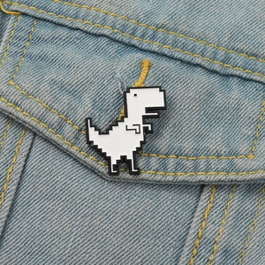 White pixel art dinosaur brooch pinned on blue denim jacket pocket as a creative accessory
