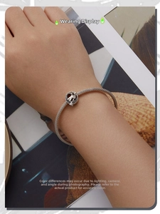Detailed view of silver mesh bracelet with hollow round charm and dark stones on wrist