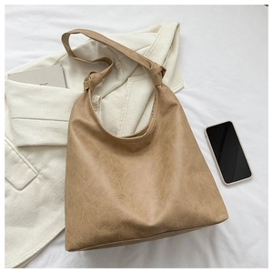 Flat lay of a caramel PU leather tote bag with knot strap detail on an ivory blazer