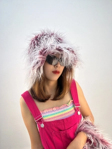 Detail of purple faux fur bucket hat paired with bright pink denim dungarees on model