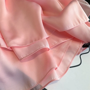 Detailed close-up of pink satin scarf texture with layered ruffle design and hemmed edges