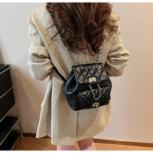Rear view of a model wearing a black quilted leather backpack with gold chain straps