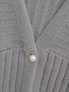 Detail of grey knitted cardigan showing soft fabric texture and decorative pearl button