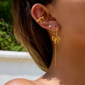 Golden bow tassel earrings and ear cuff set worn by a model in a natural outdoor setting