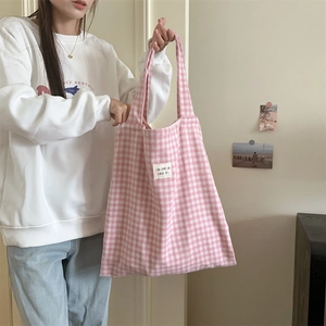 Detail of pink plaid canvas tote bag featuring white woven label and soft fabric texture