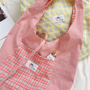 Detail of pink nylon tote bag featuring yellow plaid lining and cartoon woven label