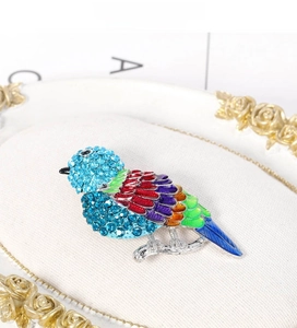 Dettaglio di spilla a uccello colorata con strass e ali in smalto su vassoio per gioielli