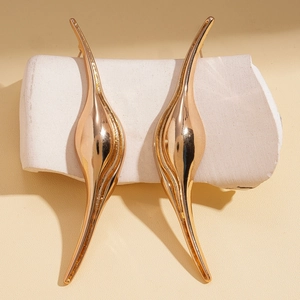 Abstract metallic leaf earrings with polished gold curved teardrop design on stone display