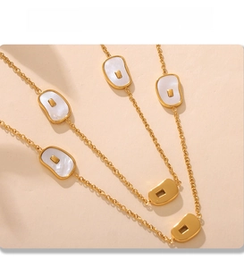 Detail of PVD gold plated long necklace with white shell pendants on a beige background