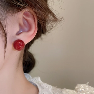 Close-up of minimalist red spherical stud earrings worn by a model in warm lighting