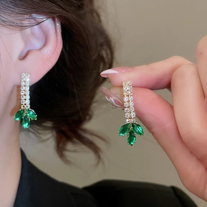 Close-up of golden tassel earrings with marquise green gems and zircons on ear