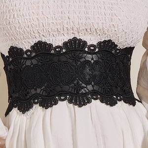 Close-up of elegant black floral lace corset belt with detailed cutout patterns on a white top