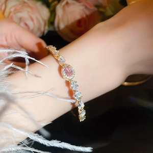 Detail of gold bracelet featuring pink oval gemstone and sparkling zircon halo