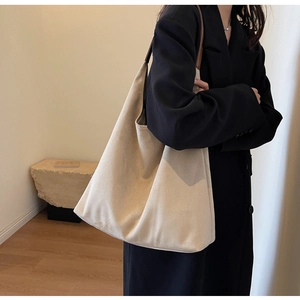 Detail of minimalist beige suede shoulder bag on model wearing a black blazer