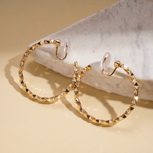 Detail of gold geometric hoop clip-on earrings with textured diamond-cut facets on marble