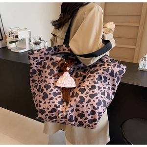 Leopard print tote bag with brown plush bunny charm shown on a model in a cafe setting