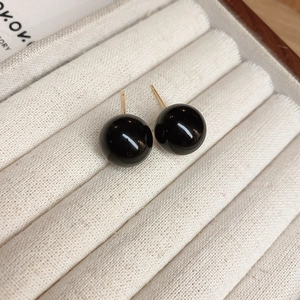 Macro detail of minimalist black bead earrings with gold pins on a velvet jewelry tray