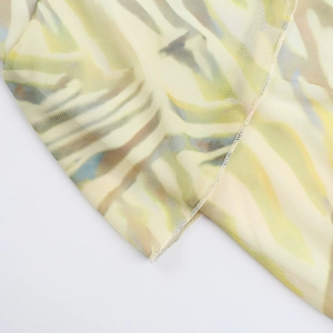 Detail of light yellow knit mesh fabric with green tropical leaf prints and fine stitching