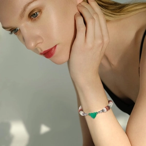 Colorful beaded bracelet with silver spacers and a green heart charm on model wrist
