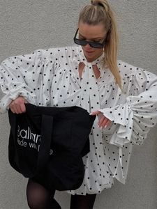 Close-up of white polka dot blouse featuring ruffled bell sleeves and tie-up bow neckline