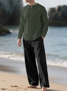 Detail eines dunkelgrünen Leinenhemdes mit schwarzer Kordelhose vor einem Strandhintergrund