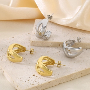 Close-up of gold and silver twisted geometric C-shaped earrings on beige stone