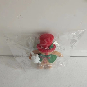 Detail of plush gingerbread man with red top hat and green vest in packaging