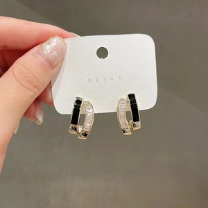 Detail of U-shaped gold earrings with black enamel and sparkling zircon stones