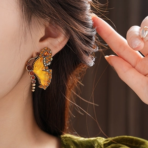 Detailed view of a vintage butterfly earring with amber and yellow crystals on a model