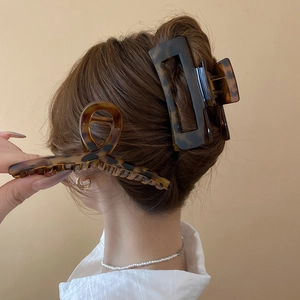 Detail view of large tortoiseshell hair claws securing a sleek bun in a minimalist setting