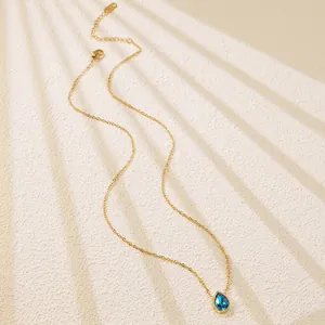 Detail of gold chain necklace with a water drop blue gemstone pendant and lobster clasp