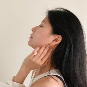Close-up of elegant gold flower studs and clover ring worn by model in warm lighting