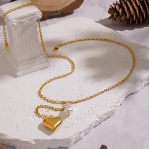 Detailed shot of 18K gold plated heart and baroque pearl pendants on a stainless steel chain