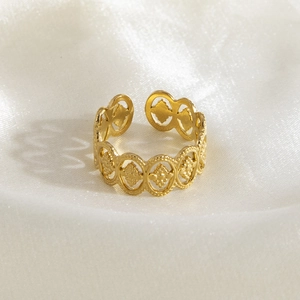 Detail of gold open ring with intricate hollow filigree pattern on white silk