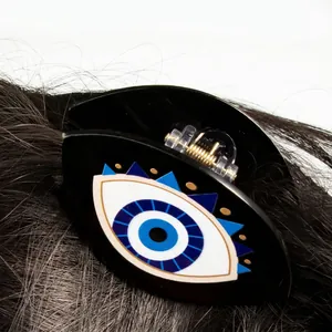 Black acrylic hair claw clip with evil eye pattern shown on dark hair texture
