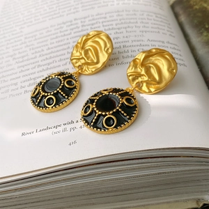 Detail of vintage round earrings with gold texture and black enamel on a book