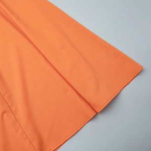 Detailed close-up of orange cotton linen fabric texture and premium stitching on the hem