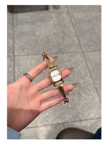 Detail shot of a luxury gold rectangular ladies' watch featuring a white dial and metal strap