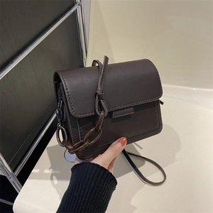 Detail van donkerbruine vierkante crossbodytas met chique dikke kettingaccenten