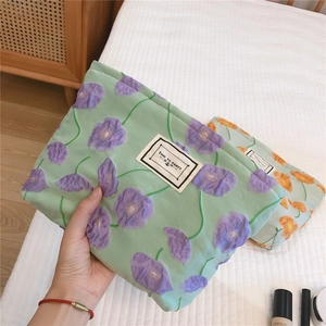 Close-up of a quilted floral makeup bag in light green with purple poppy patterns