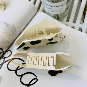 Détail de la pince à cheveux en acrylique crème à motifs verts sur un livre décoratif