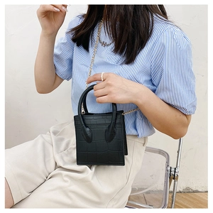 Detail of black crocodile texture mini bag with gold chain strap on a model