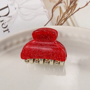 Close-up of a stylish red glitter acrylic hair claw clip in a white ceramic tray