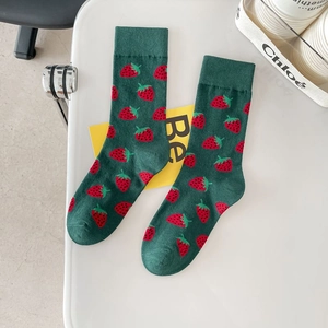 Dark green crew socks with vibrant red strawberry patterns on a minimalist desk