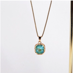 Detailed close-up of teal square gem pendant with golden lace filigree on box chain