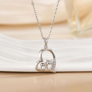 Silver heart necklace with owls and sparkling crystals on a white ceramic tray