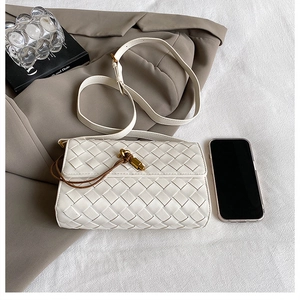 Detail of woven beige crossbody bag with gold knot lock next to smartphone for scale